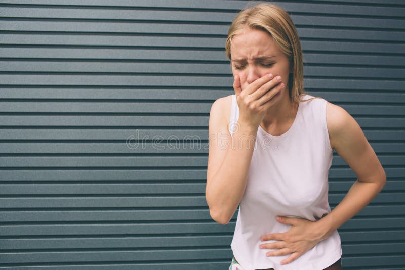 Young woman with hands on stomach having bad aches pain on gray background. Food poisoning, influenza, cramps. Health issues problems concept. Young woman with hands on stomach having bad aches pain on gray background. Food poisoning, influenza, cramps. Health issues problems concept