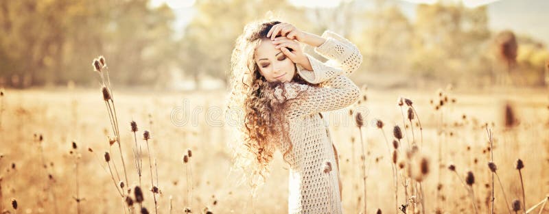 Jovem mulher com o cabelo encaracolado bonito que levanta no campo no por do sol fotografia de stock royalty free Jovem mulher com o cabelo encaracolado bonito que levanta no campo no por do sol fotografia de stock royalty free
