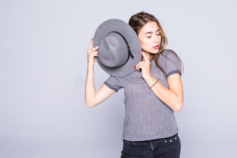 Jovem mulher com o chap?u nas m?os que possing no fundo cinzento fotografia de stock royalty free Jovem mulher com o chap?u nas m?os que possing no fundo cinzento fotografia de stock royalty free