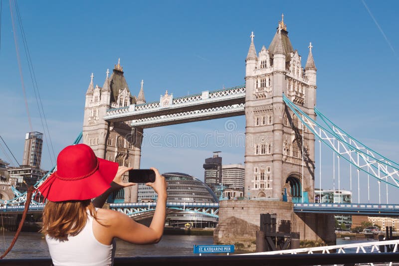 Jovem mulher com o chap?u vermelho que toma uma foto da ponte da torre em Londres imagem de stock Jovem mulher com o chap?u vermelho que toma uma foto da ponte da torre em Londres imagem de stock