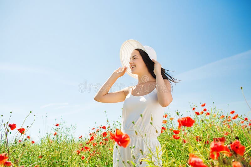 A jovem mulher de sorriso no chapéu de palha na papoila coloca fotos de stock royalty free A jovem mulher de sorriso no chapéu de palha na papoila coloca fotos de stock royalty free