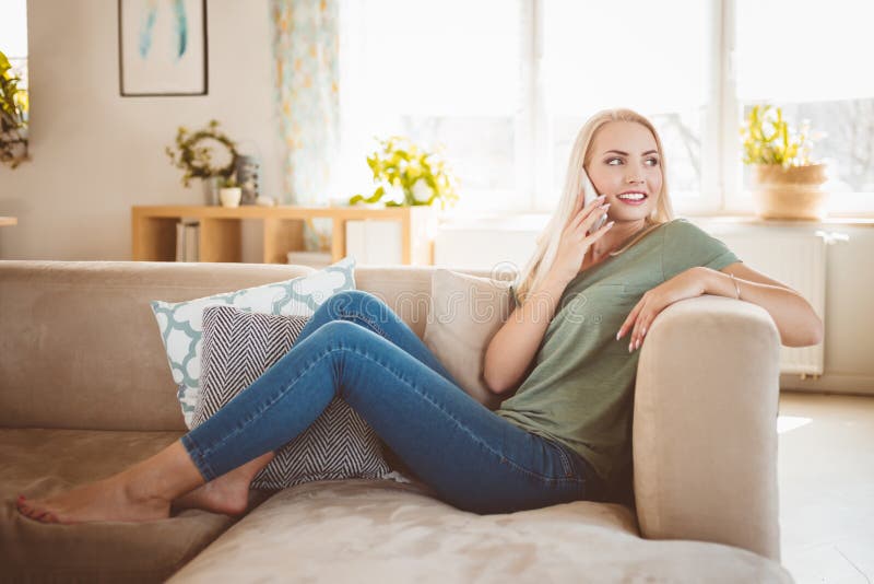 Garota feliz com telefone relaxa no sofá ou no sofá da sala