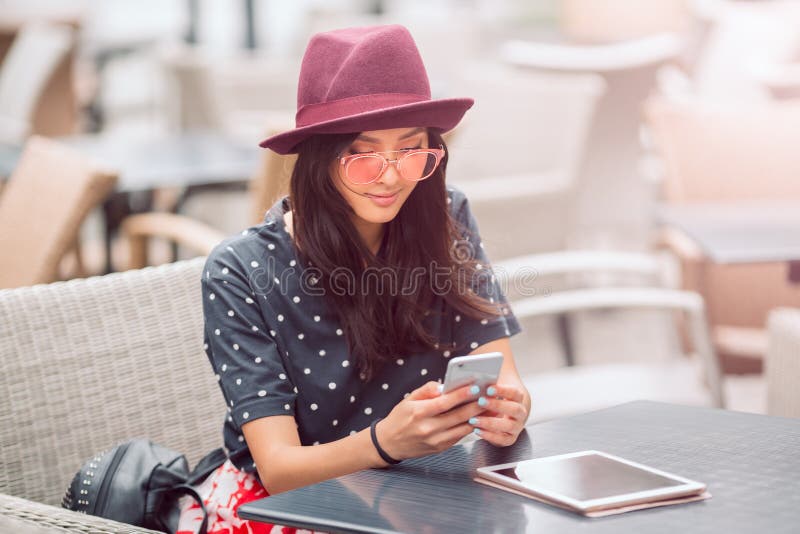 A jovem mulher de sorriso que olha o telefone esperto no café compra fotos de stock royalty free A jovem mulher de sorriso que olha o telefone esperto no café compra fotos de stock royalty free
