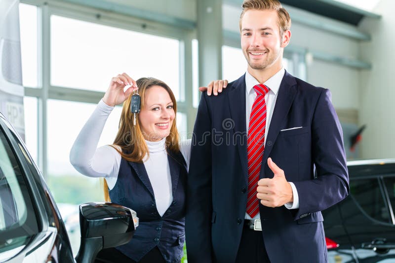 Sellers or car salesman and female customer in dealership, the women holding the key in the hand and is pleased about the purchase of the auto or new car. Sellers or car salesman and female customer in dealership, the women holding the key in the hand and is pleased about the purchase of the auto or new car