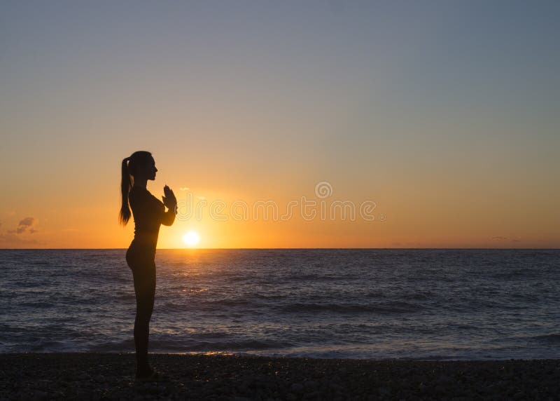 Jovem mulher em uma pose meditando da ioga que negligencia o por do sol bonito Conceito do espírito do corpo da mente imagem de stock royalty free Jovem mulher em uma pose meditando da ioga que negligencia o por do sol bonito Conceito do espírito do corpo da mente imagem de stock royalty free
