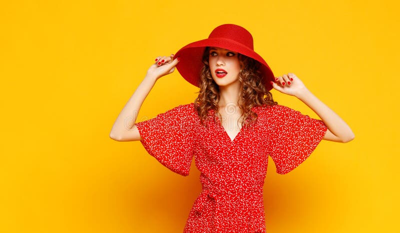 Jovem mulher emocional feliz do conceito no vestido vermelho e no chapéu do verão que saltam no fundo amarelo imagem de stock Jovem mulher emocional feliz do conceito no vestido vermelho e no chapéu do verão que saltam no fundo amarelo imagem de stock