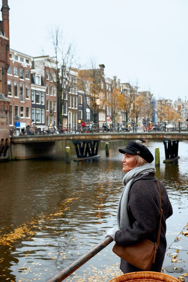 A jovem mulher está na ponte e olha o canal de Amsterdão, Países Baixos fotos de stock royalty free A jovem mulher está na ponte e olha o canal de Amsterdão, Países Baixos fotos de stock royalty free