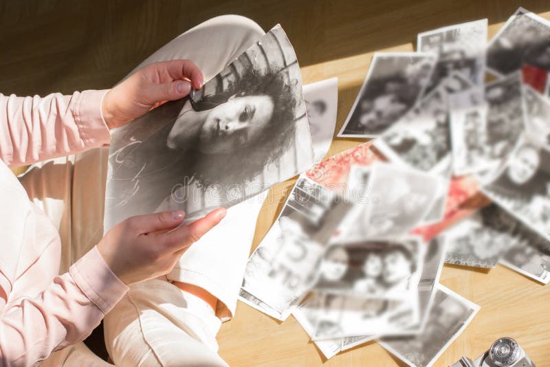 A jovem mulher está sentando-se no assoalho e está olhando-se fotografias preto e branco imagens de stock A jovem mulher está sentando-se no assoalho e está olhando-se fotografias preto e branco imagens de stock
