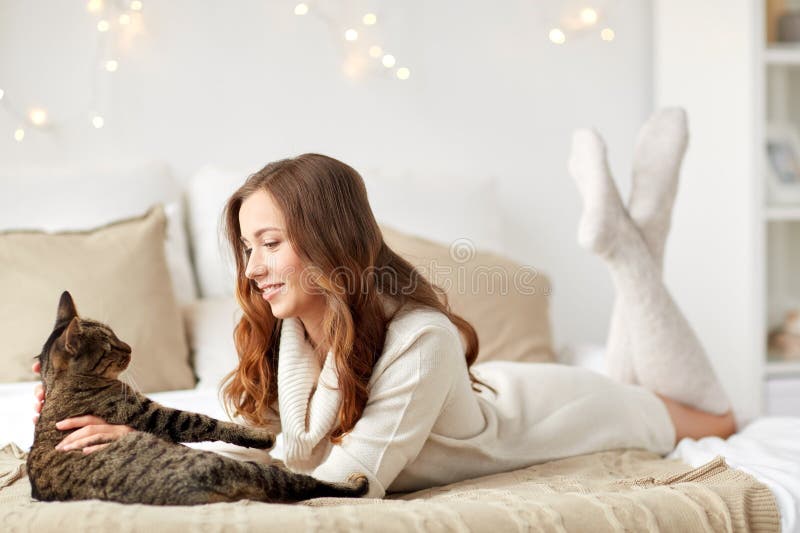 Jovem mulher feliz com o gato que encontra-se na cama em casa