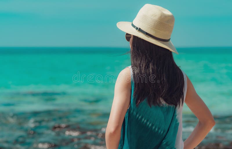 Jovem mulher feliz na forma do estilo ocasional e na posição do chapéu de palha na praia do mar Relaxando e para apreciar o feria foto de stock Jovem mulher feliz na forma do estilo ocasional e na posição do chapéu de palha na praia do mar Relaxando e para apreciar o feria foto de stock