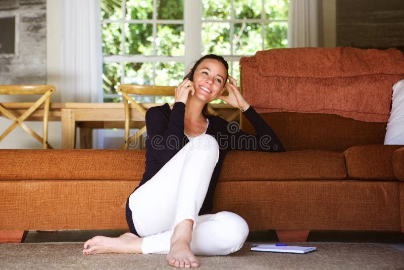 Jovem mulher feliz na sala de visitas usando o telefone celular imagens de stock royalty free Jovem mulher feliz na sala de visitas usando o telefone celular imagens de stock royalty free