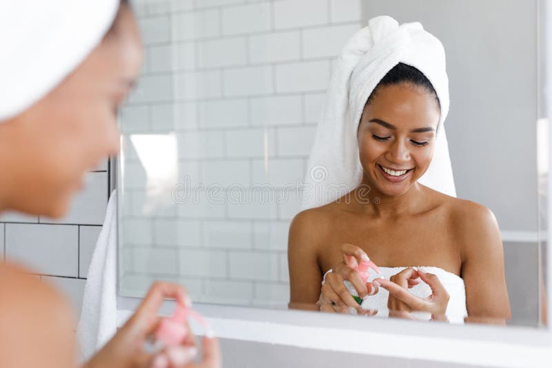 Jovem mulher feliz que aplica o creme de cara no banheiro foto de stock Jovem mulher feliz que aplica o creme de cara no banheiro foto de stock