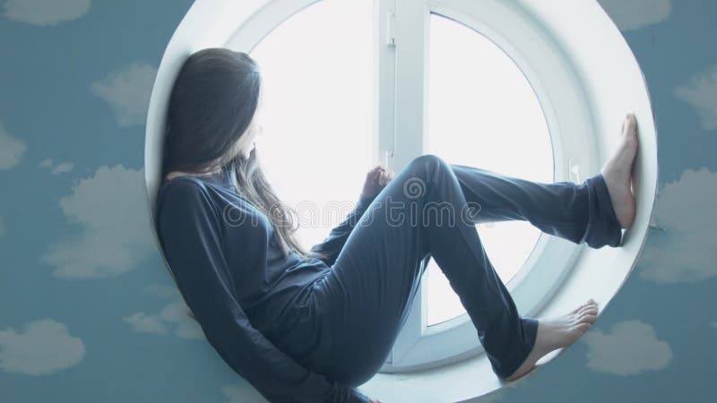 A jovem mulher feliz relaxa em uma janela redonda Uma menina bonita de sorriso em uma janela em uma sala azul Papéis de parede co