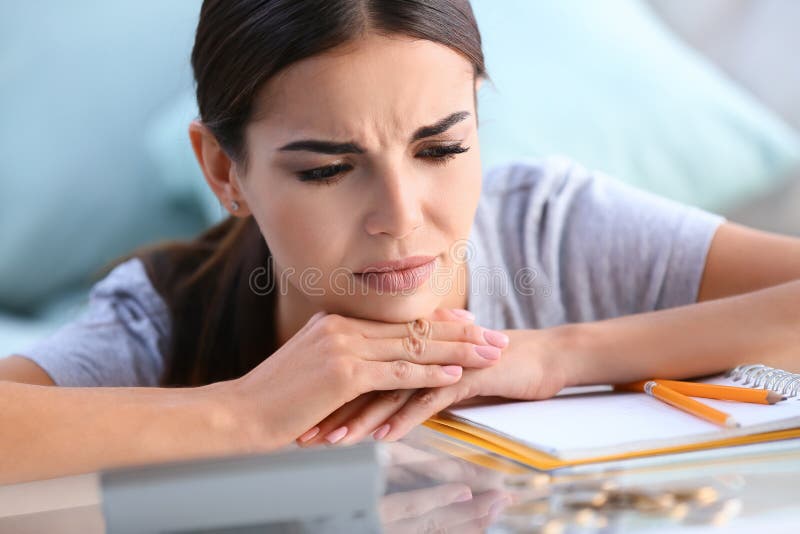 Jovem mulher incomodada que pensa sobre contas ao sentar-se na tabela fotos de stock royalty free Jovem mulher incomodada que pensa sobre contas ao sentar-se na tabela fotos de stock royalty free