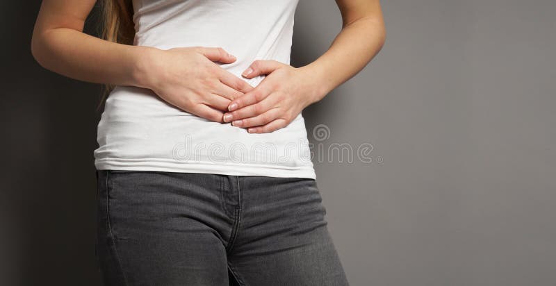 Midsection of unrecognizable young woman holding her stomach with both hands - concept for dysmenorrhea, abdominal pain, irritable bowel syndrome, bellyache, stomachache, painful periods or menstrual cramps. Midsection of unrecognizable young woman holding her stomach with both hands - concept for dysmenorrhea, abdominal pain, irritable bowel syndrome, bellyache, stomachache, painful periods or menstrual cramps