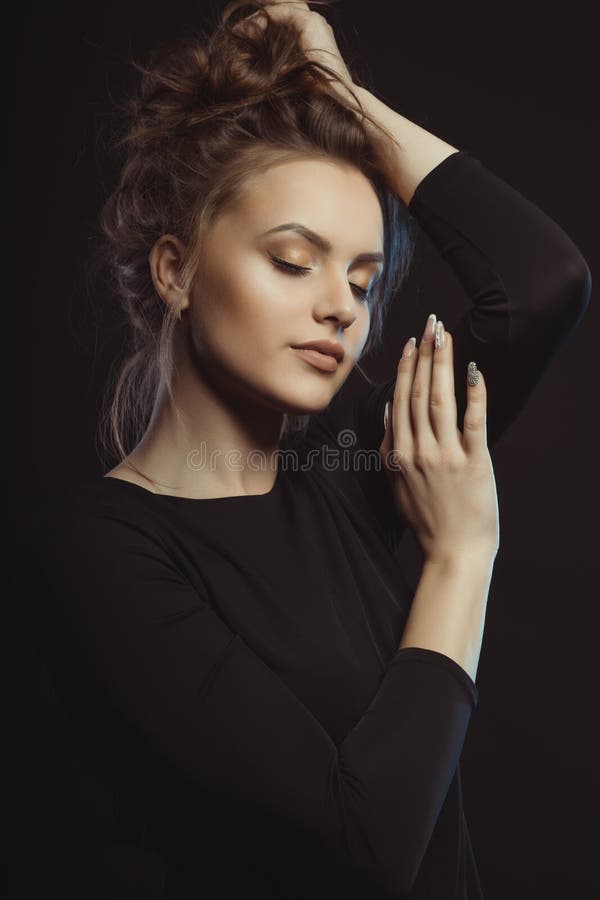 Jovem mulher luxuoso no vestido preto que levanta no estúdio imagem de stock Jovem mulher luxuoso no vestido preto que levanta no estúdio imagem de stock