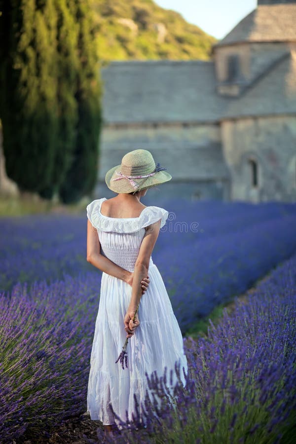 Romantic lady in lavender field. An ancient monastry in background. Wearing white dress and light green hat, holding some lavender twigs in her hand. Relaxing and enjoying. Romantic lady in lavender field. An ancient monastry in background. Wearing white dress and light green hat, holding some lavender twigs in her hand. Relaxing and enjoying.