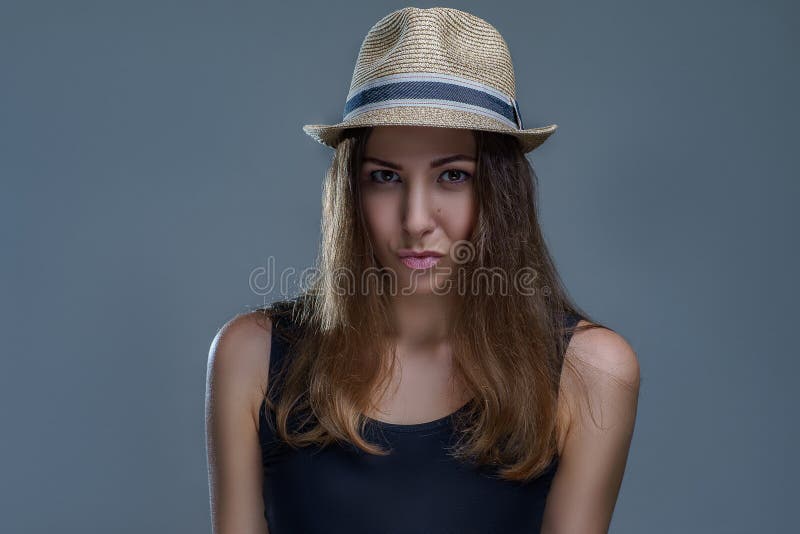 A jovem mulher no chapéu e na camisa preta levantando 'sexy' está sendo isolada no fundo cinzento em um fim do estúdio acima imagem de stock royalty free A jovem mulher no chapéu e na camisa preta levantando 'sexy' está sendo isolada no fundo cinzento em um fim do estúdio acima imagem de stock royalty free