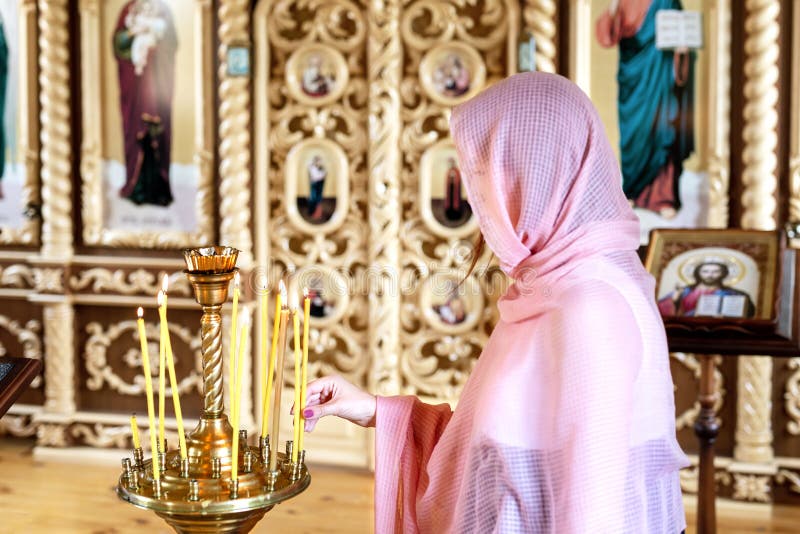 Jovem mulher no lenço cor-de-rosa que reza perto das velas na igreja de madeira Deus da adoração da pessoa fêmea no templo fotos de stock royalty free Jovem mulher no lenço cor-de-rosa que reza perto das velas na igreja de madeira Deus da adoração da pessoa fêmea no templo fotos de stock royalty free
