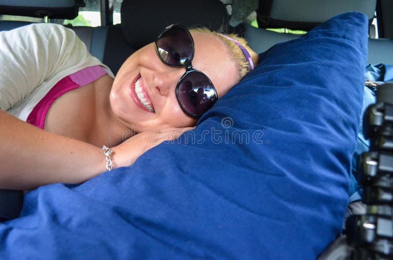 A jovem mulher obtém confortável no assento traseiro de um carro, com um grande descanso, apronta-se à sesta em uma viagem de lon fotos de stock royalty free A jovem mulher obtém confortável no assento traseiro de um carro, com um grande descanso, apronta-se à sesta em uma viagem de lon fotos de stock royalty free
