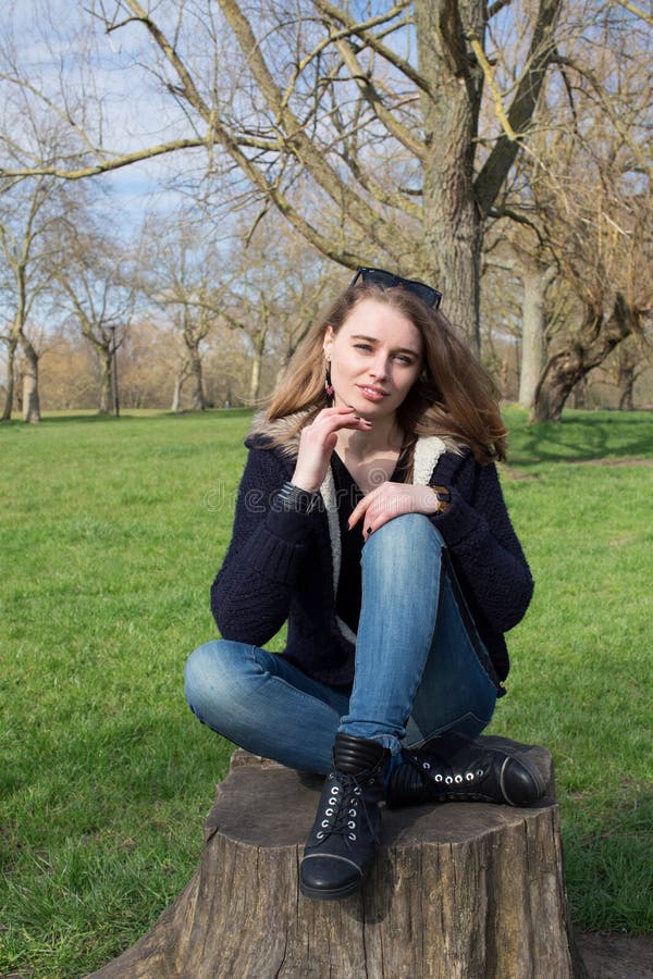Jovem mulher pensativa que senta-se em um coto de árvore velho imagens de stock Jovem mulher pensativa que senta-se em um coto de árvore velho imagens de stock