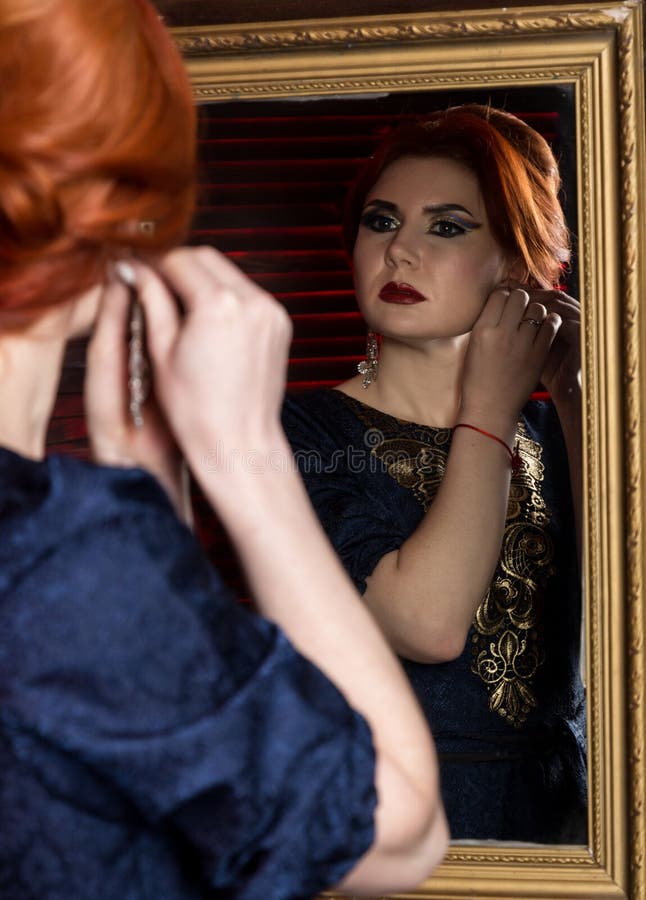 A jovem mulher põe sobre brincos bonitos na frente do espelho Menina bonita no estilo do vintage imagem de stock A jovem mulher põe sobre brincos bonitos na frente do espelho Menina bonita no estilo do vintage imagem de stock