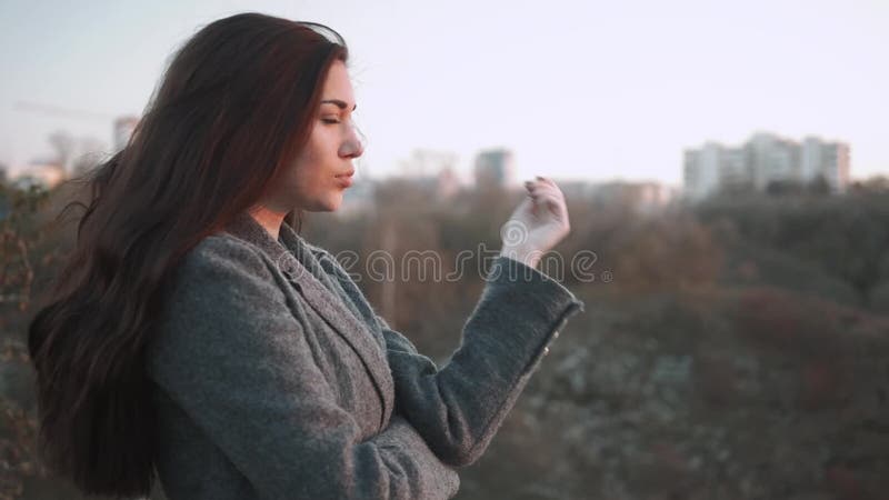 Jovem mulher que aquece-se no outono Dia frio da queda Gelo da mulher no por do sol na rua com fundo da cidade