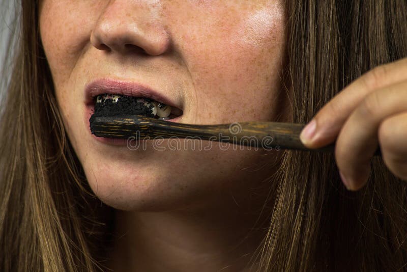 Jovem mulher que escova seus dentes com uma pasta de dente preta com carvão vegetal ativo, e escova de dentes do preto no fundo b fotografia de stock royalty free Jovem mulher que escova seus dentes com uma pasta de dente preta com carvão vegetal ativo, e escova de dentes do preto no fundo b fotografia de stock royalty free
