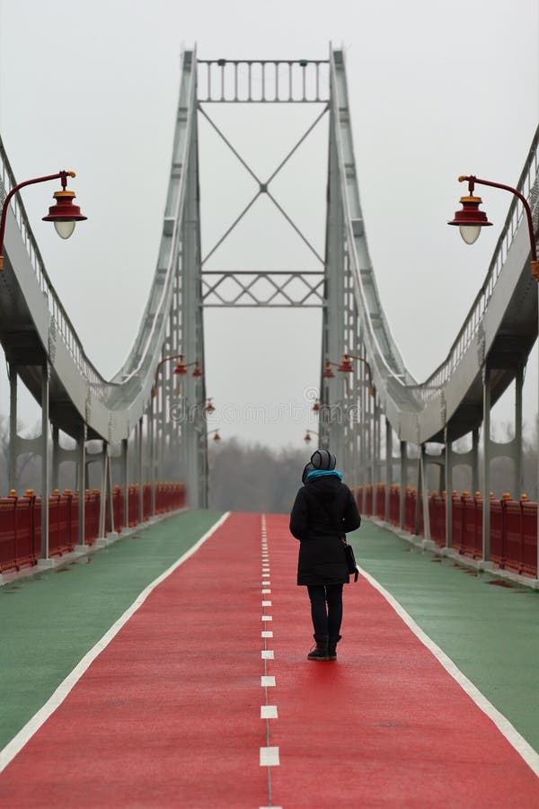 Jovem mulher que está e que espera em um dia nevoento chuvoso na ponte pedestre do centro da cidade de Kyiv imagens de stock royalty free Jovem mulher que está e que espera em um dia nevoento chuvoso na ponte pedestre do centro da cidade de Kyiv imagens de stock royalty free