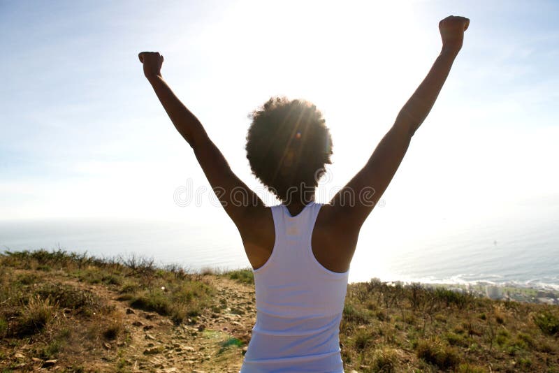Rear view portrait of young woman standing on cliff with her hands raised towards sky and looking at the sea. Rear view portrait of young woman standing on cliff with her hands raised towards sky and looking at the sea