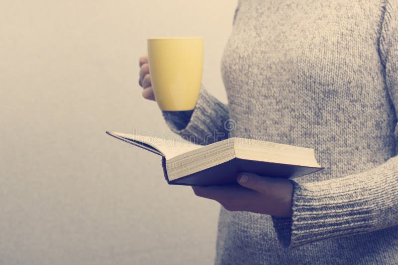 Jovem mulher que lê um livro e que guarda o copo do chá fotografia de stock Jovem mulher que lê um livro e que guarda o copo do chá fotografia de stock