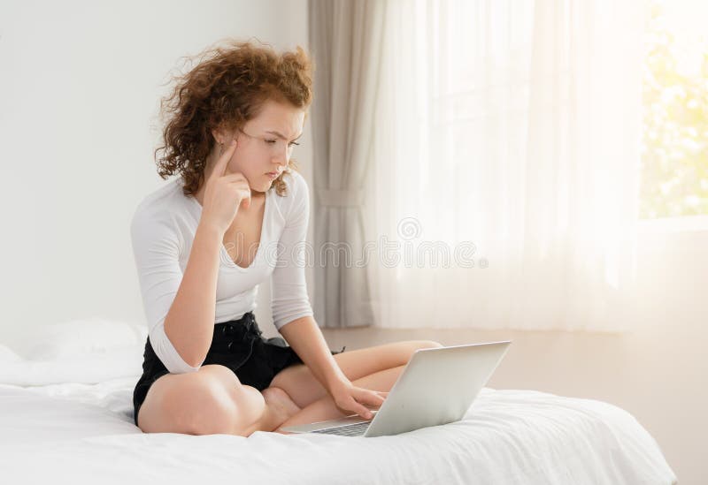 A jovem mulher que senta-se na cama no quarto com seu port?til tem um problema fotos de stock royalty free A jovem mulher que senta-se na cama no quarto com seu port?til tem um problema fotos de stock royalty free