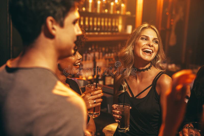 Beautiful young women having drink at nightclub with friends. Group of people enjoying party in pub. Beautiful young women having drink at nightclub with friends. Group of people enjoying party in pub.