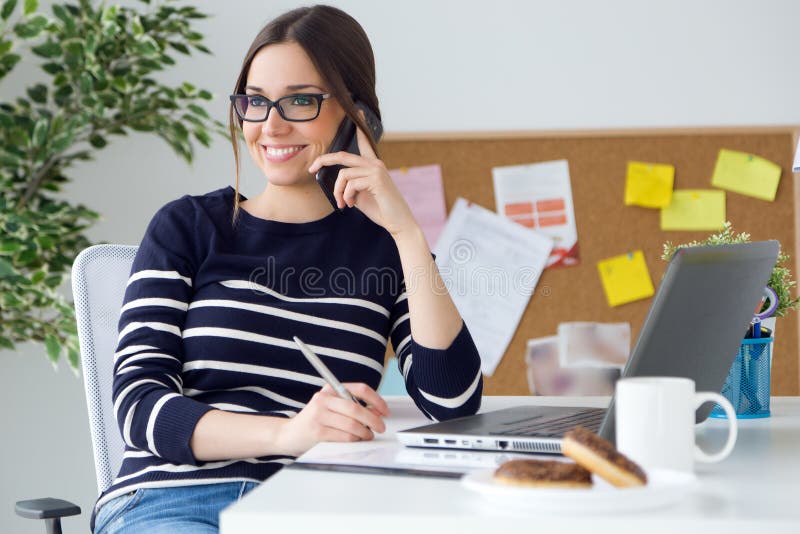 Jovem mulher segura que trabalha em seu escritório com telefone celular fotos de stock royalty free Jovem mulher segura que trabalha em seu escritório com telefone celular fotos de stock royalty free