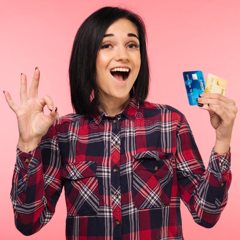 A jovem mulher surpreendida entusiasmado alegre com exibição do cartão de crédito canta está bem sobre o fundo cor-de-rosa fotos de stock royalty free A jovem mulher surpreendida entusiasmado alegre com exibição do cartão de crédito canta está bem sobre o fundo cor-de-rosa fotos de stock royalty free