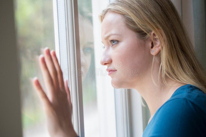 Jovem mulher triste que sofre da depressão que olha fora da janela foto de stock Jovem mulher triste que sofre da depressão que olha fora da janela foto de stock