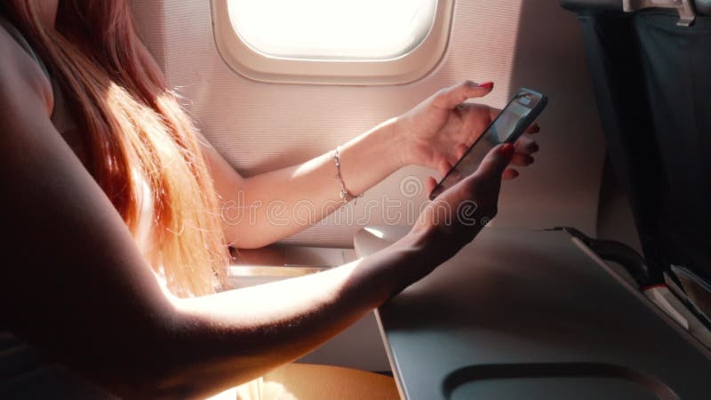 A jovem mulher usa um smartphone durante um voo do avião