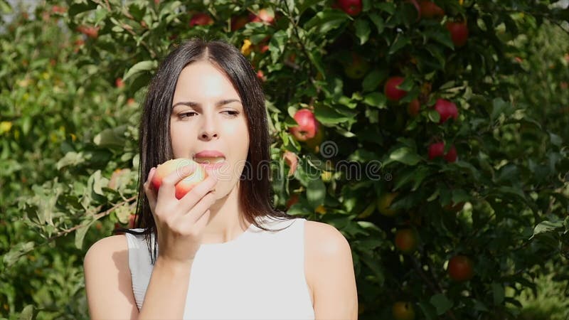 A jovem mulher vestiu-se em um vestido branco que gira em torno e que levanta na câmera na frente do sol na Apple-árvore