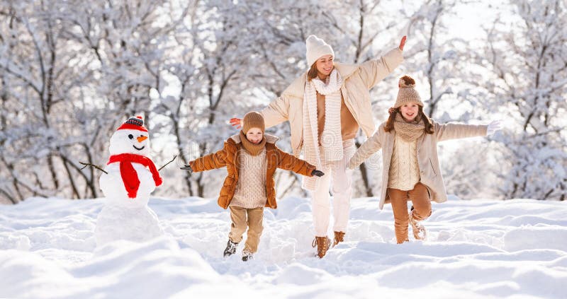 Jovem mãe de família positiva e dois filhos pequenos correndo alegremente pela neve branca no parque de inverno