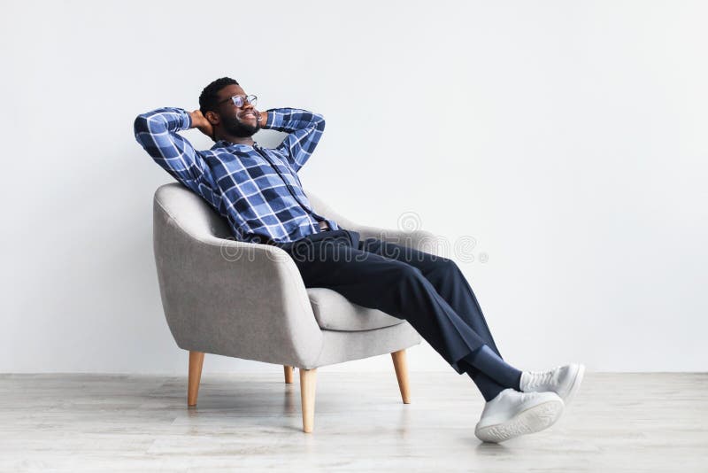 Jovem negro pacífico relaxando em poltrona contra o espaço livre do estúdio branco