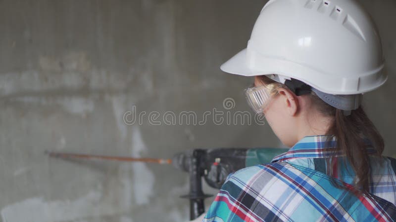 Jovem operário de construção de uma parede de concreto com a perfuração