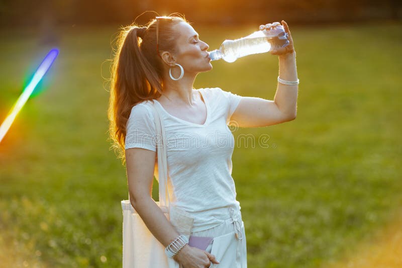 Summer time. relaxed young woman in white shirt with bottle of water in the meadow in the city park. Summer time. relaxed young woman in white shirt with bottle of water in the meadow in the city park