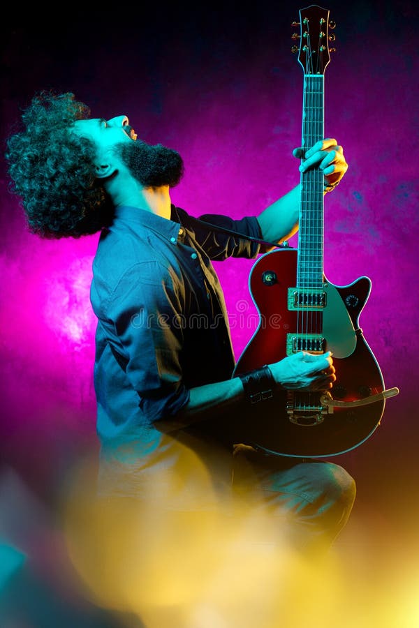 Jovem rocker hipster com cabelo encaracolado com guitarra vermelha em luzes de neon Músico de rock tocando violão elétrico fotos de stock royalty free Jovem rocker hipster com cabelo encaracolado com guitarra vermelha em luzes de neon Músico de rock tocando violão elétrico fotos de stock royalty free