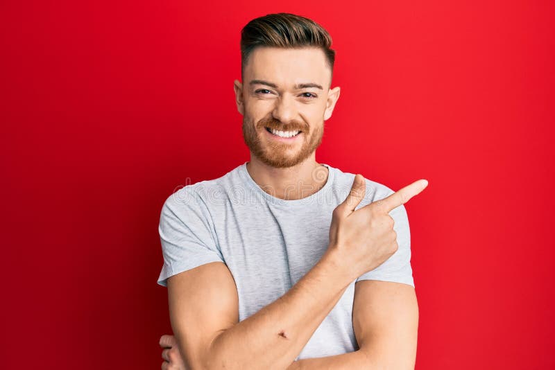 Young redhead man wearing casual grey t shirt smiling cheerful pointing with hand and finger up to the side. Young redhead man wearing casual grey t shirt smiling cheerful pointing with hand and finger up to the side