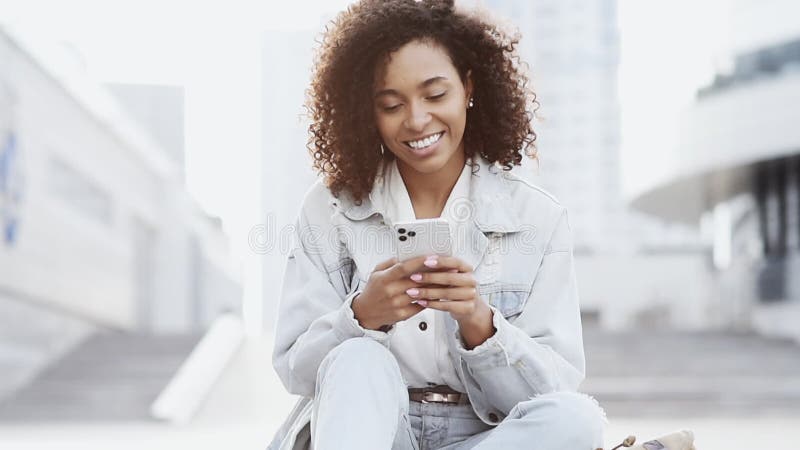 Jovem sorridente usando smartphone em uma cidade. estudante de garotas mandando um celular para fora.