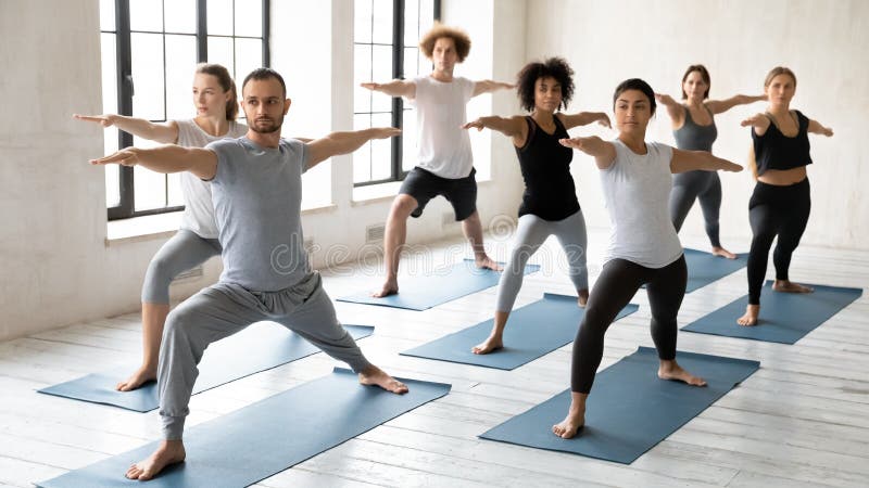 Jovem treinador masculino líder na classe yoga para estudantes multirraciais concentrados.