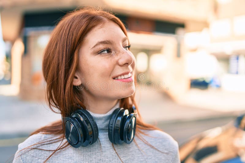 Joven adolescente irlandesa sonriendo feliz usando auriculares en la ciudad fotografía de archivo