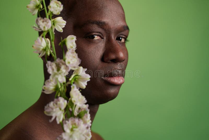 Joven africano posando con flores. Armario de una modelo africana sin camisa mirando la cámara mientras posa con flores sobre el fondo verde