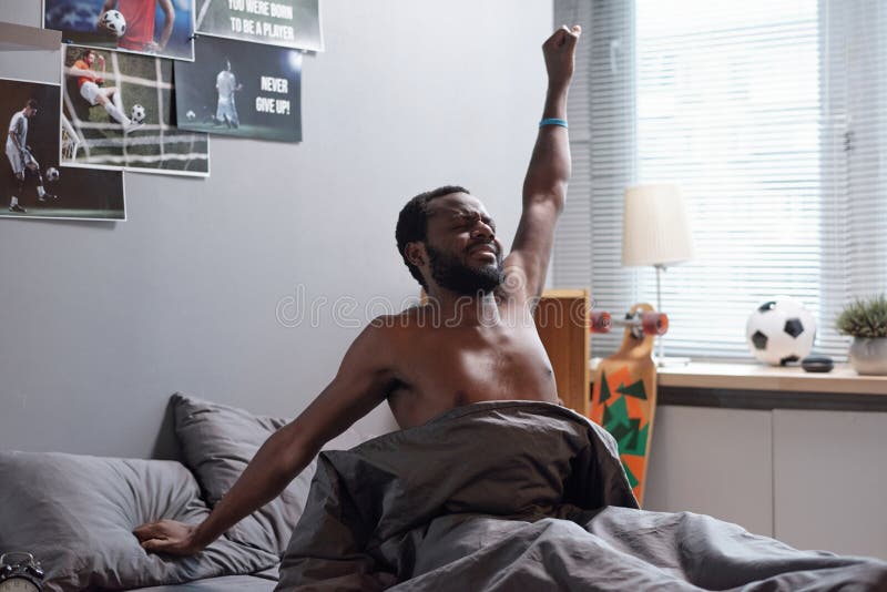 Joven africano sin camisa estirándose en la cama después de despertarse fotos de archivo libres de regalías