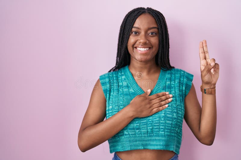 Joven afroamericano con trenzas paradas sobre un fondo rosado sonriendo jurando con la mano en el pecho y los dedos haciendo un imágenes de archivo libres de regalías